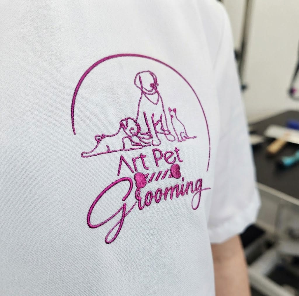 Close-up of a white shirt with "Art Pet Grooming" and pet outlines embroidered in pink, perfect for professional pet groomers or those offering mobile cat grooming and mobile dog grooming services.